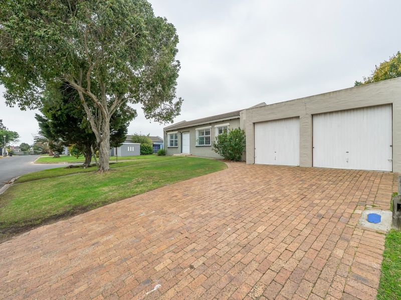 Front exterior view of a single-story house featuring a double garage, brick paved driveway, and established front garden.