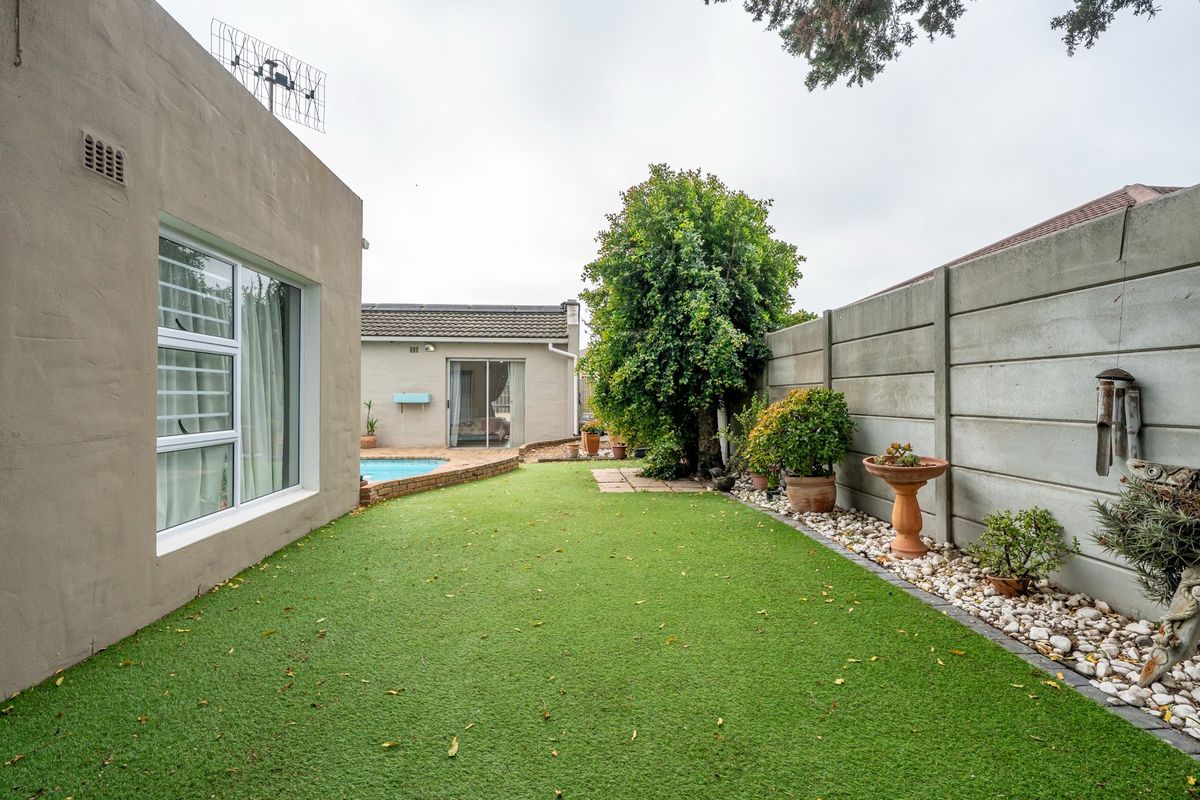 Rear garden area featuring an artificial lawn, swimming pool, and precast concrete boundary wall, providing a low-maintenance outdoor space.
