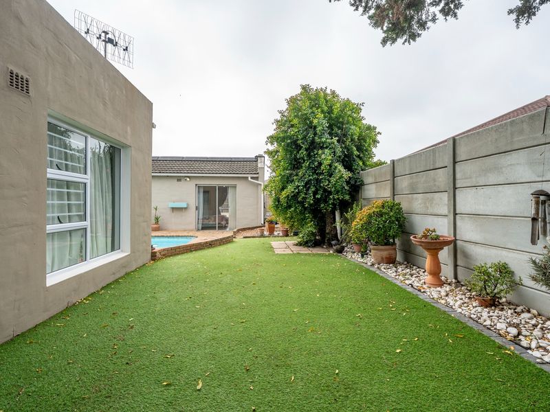 Rear garden area featuring an artificial lawn, swimming pool, and precast concrete boundary wall, providing a low-maintenance outdoor space.