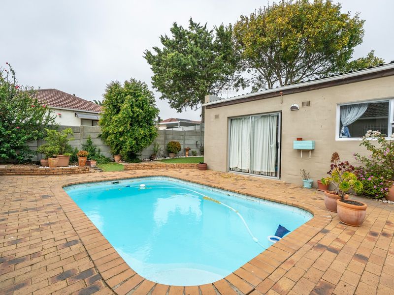 Rear garden area featuring a swimming pool with brick paving surround, enclosed by a precast concrete boundary wall and accessible via sliding glass doors.