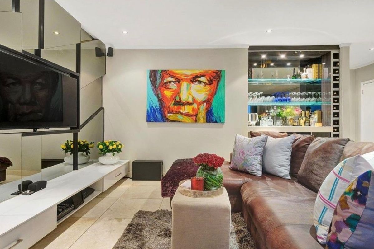 A modern living room featuring tiled flooring, recessed downlights, a mirrored feature wall, and a built-in bar area with glass shelving.