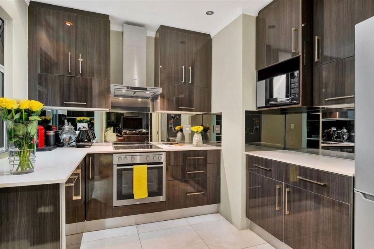 Modern kitchen featuring dark wood-grain cabinetry, stone countertops, a reflective mirror splashback, and integrated stainless steel appliances including an oven and extractor fan.