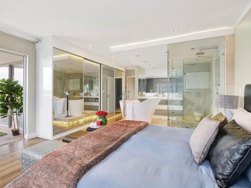 Spacious master bedroom featuring an open-plan en-suite bathroom with a glass shower, freestanding tub, and extensive mirrored built-in wardrobes, leading to a private balcony.
