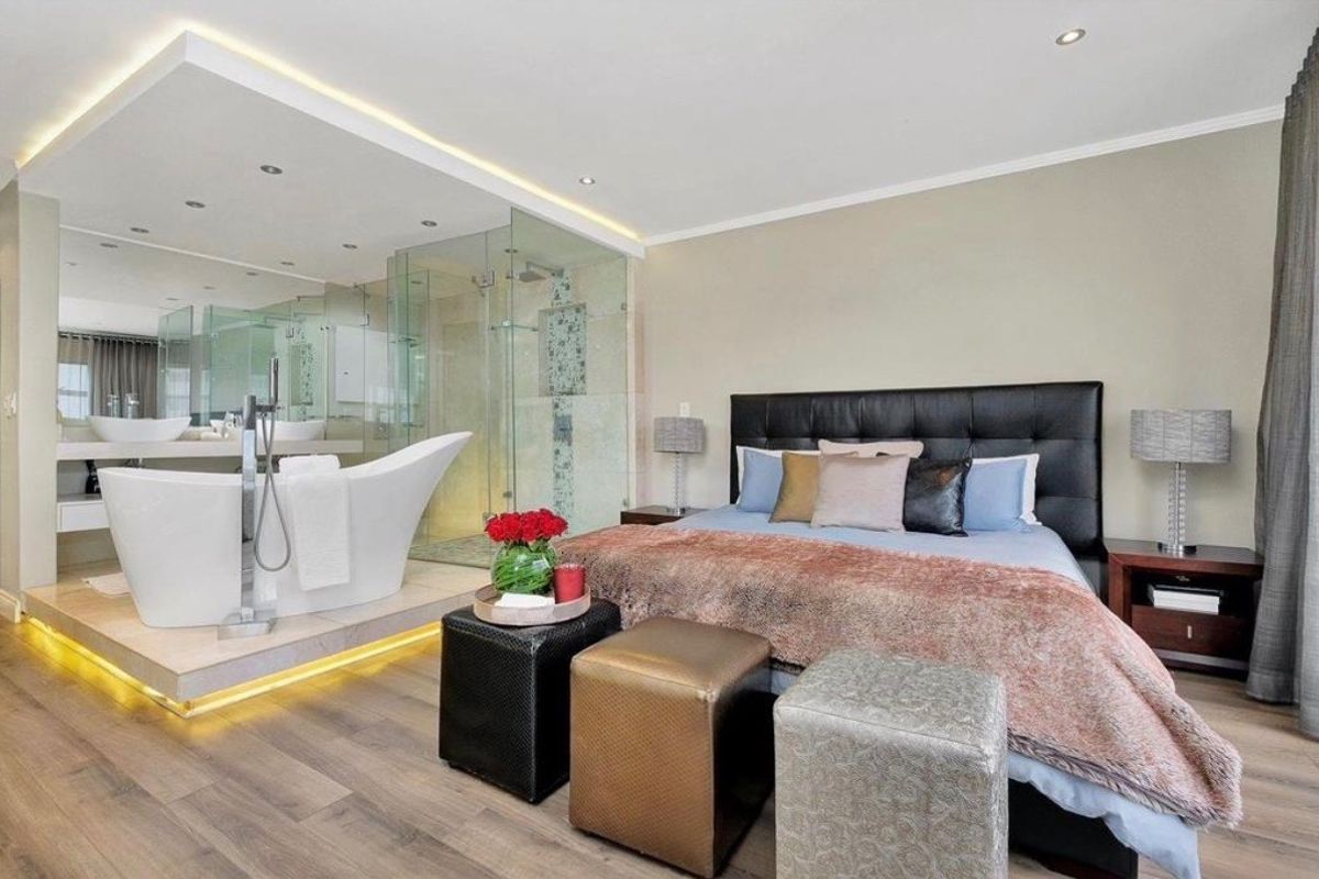 A modern open-plan bedroom featuring an integrated en-suite bathroom with a freestanding bathtub, glass shower, and premium finishes.