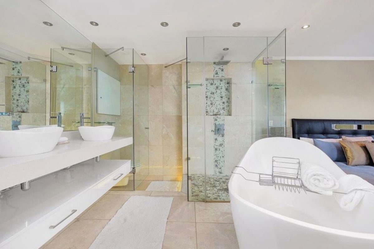 Modern open-plan bathroom featuring a sleek double vanity, a contemporary freestanding bathtub, and a spacious glass-enclosed shower with stone tile finishes.