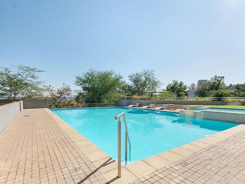 A well-maintained outdoor swimming pool area featuring a paved deck, stainless steel ladder, and perimeter retaining walls with metal railings.