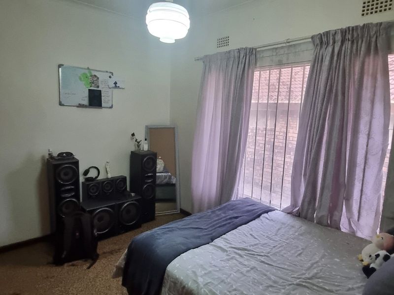 A bedroom featuring built-in cupboards and security bars on the window. The room requires cosmetic updates to flooring and finishes.