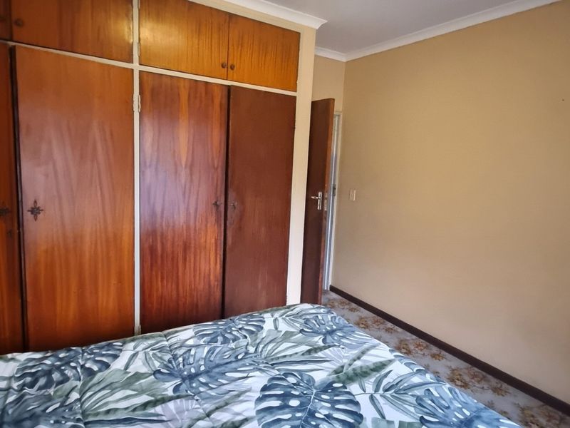 A bedroom featuring floor-to-ceiling built-in wooden cupboards and neutral wall finishes, offering a functional space with potential for modernization.