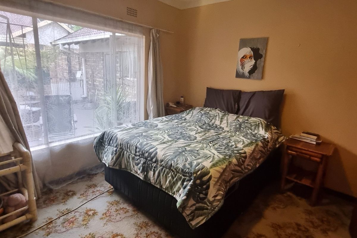 A bedroom featuring a large sliding window providing natural light and a built-in wardrobe, with dated carpet flooring in need of replacement.