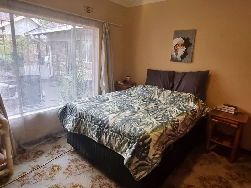 A bedroom featuring a large sliding window providing natural light and a built-in wardrobe, with dated carpet flooring in need of replacement.
