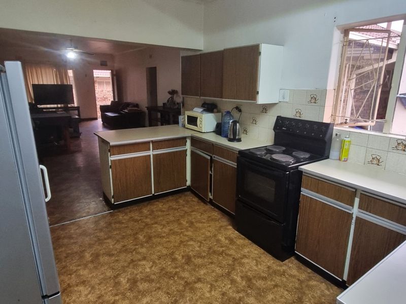 Open-plan kitchen featuring dated laminate cabinetry and countertops, flowing into the adjacent living area with vinyl flooring throughout.