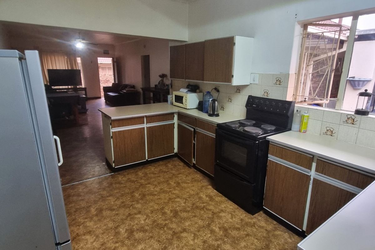 Open-plan kitchen featuring dated laminate cabinetry and countertops, flowing into the adjacent living area with vinyl flooring throughout.