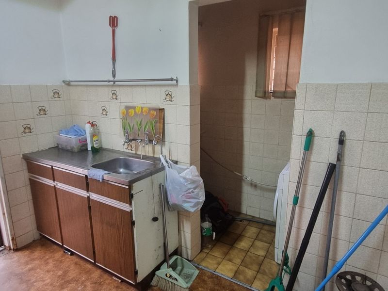 A functional laundry area featuring a stainless steel sink, tiled splashbacks, and built-in cabinetry with direct access to the exterior via a security gate.