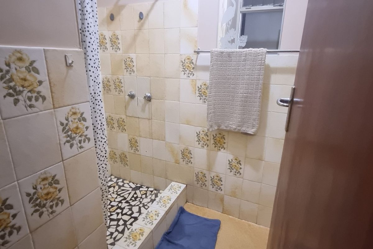 A dated bathroom featuring a tiled shower enclosure with vintage floral wall tiles and a standard shower mixer.