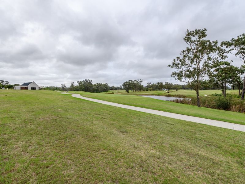 A scenic view of a well-maintained residential estate featuring a concrete pathway, manicured lawns, and a small pond.