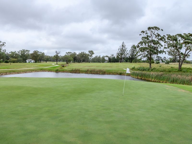 A scenic view overlooking a well-maintained golf course green with a water hazard and surrounding landscape.
