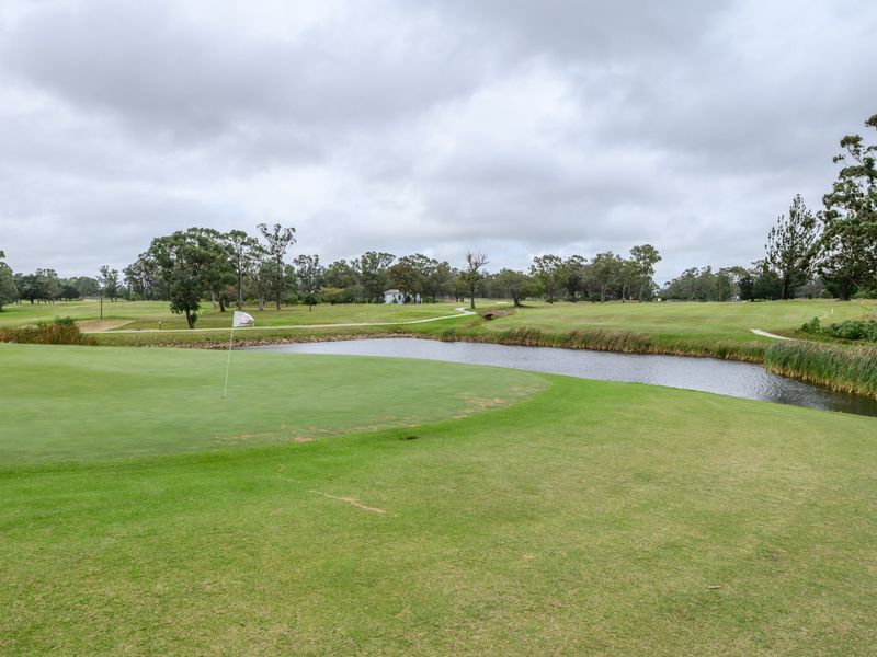A scenic view of a well-maintained golf course featuring a putting green, flag, and a water hazard set against a natural landscape.