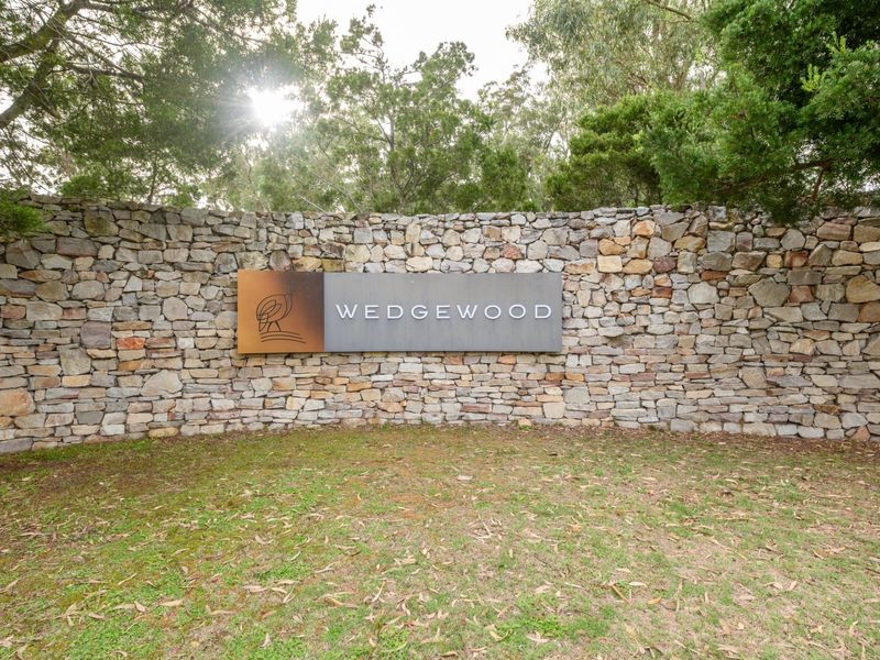 A well-maintained stone boundary wall featuring the Wedgewood estate signage, set against a backdrop of mature trees.