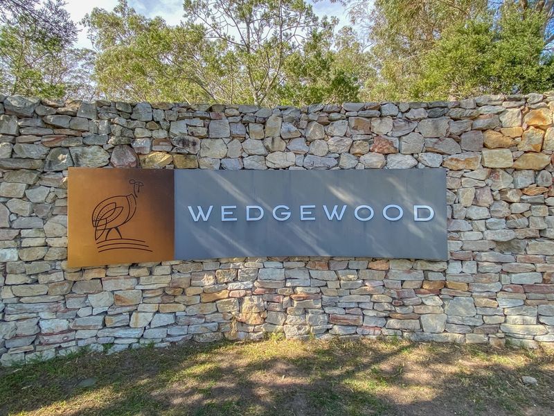 A well-maintained stone feature wall displaying the Wedgewood estate signage, set against a backdrop of mature trees.