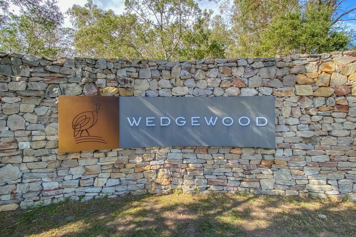 A well-maintained stone feature wall displaying the Wedgewood estate signage, set against a backdrop of mature trees.