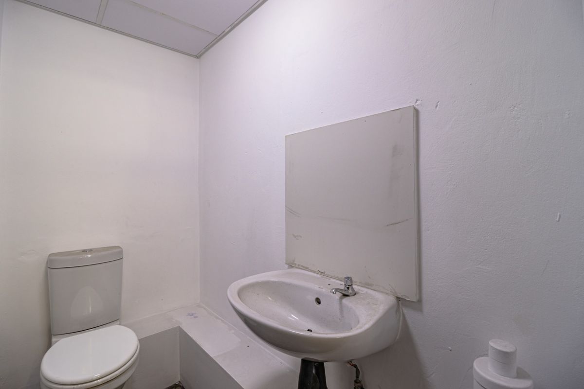 A basic commercial bathroom featuring a pedestal basin, toilet, and wall-mounted mirror, requiring cosmetic updates and maintenance.