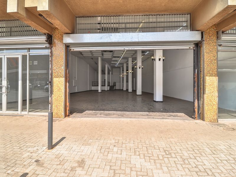 Commercial storefront featuring a wide roller shutter entrance, paved exterior walkway, and large glass display windows suitable for retail or office use.
