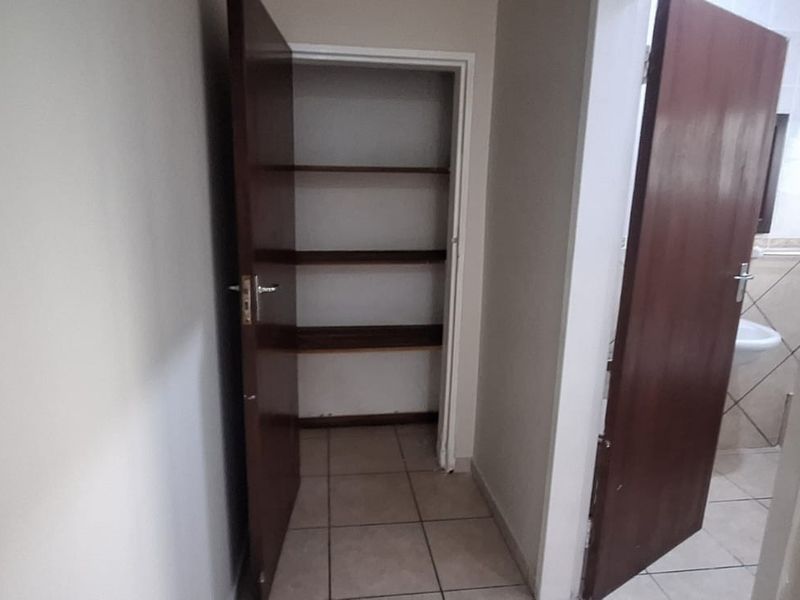 A functional hallway area featuring tiled flooring, built-in storage shelving, and access to adjacent rooms through solid core doors.