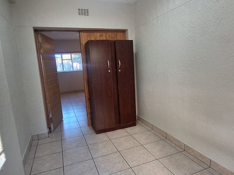 A bedroom featuring tiled flooring, venetian blinds, and a ventilation grille, showing signs of wear on the walls and floor.