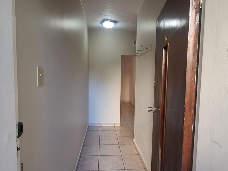 A functional apartment entrance hallway featuring tiled flooring, a ceiling light, and wall-mounted hooks, leading into the main living area.