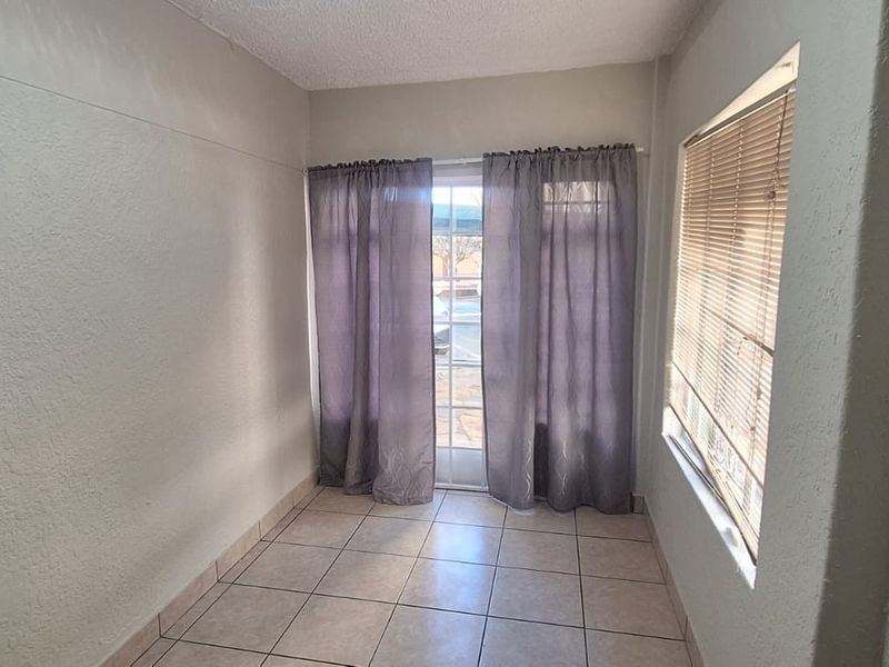 An empty, neutrally painted living area featuring tiled flooring, a glass sliding door, and a window with fitted blinds.