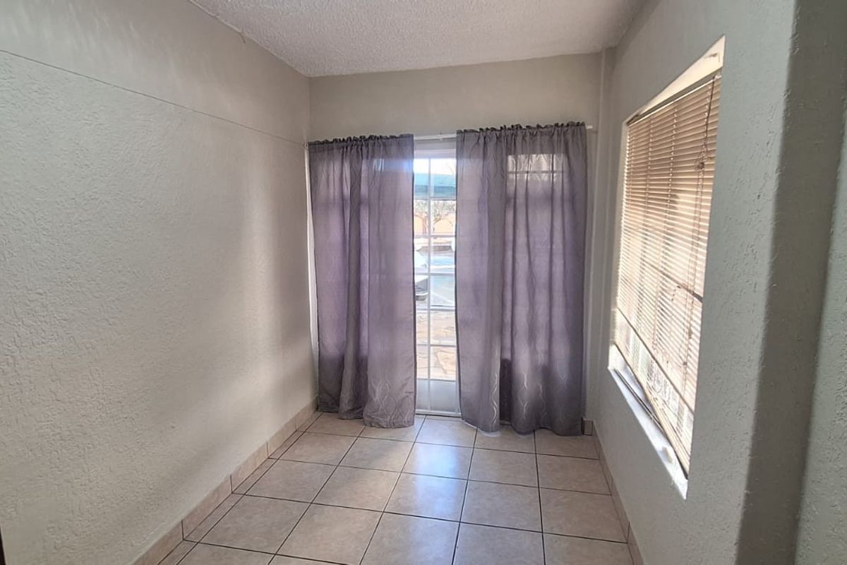 An empty, neutrally painted living area featuring tiled flooring, a glass sliding door, and a window with fitted blinds.