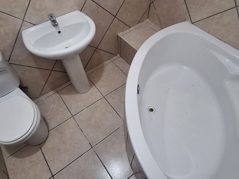 A functional bathroom featuring a corner bathtub, pedestal basin, and toilet with neutral ceramic wall and floor tiling.