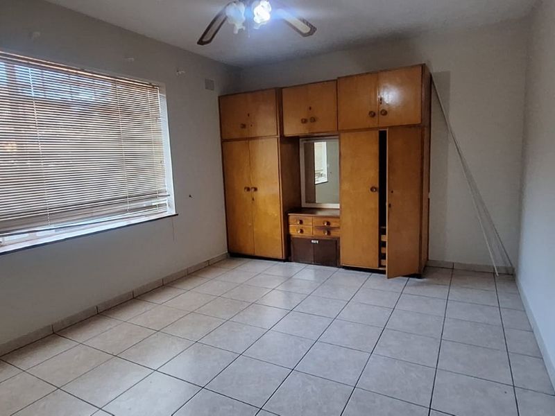 A vacant bedroom featuring tiled flooring, built-in wooden cupboards, and venetian blinds, offering a blank canvas for potential updates and personalization.