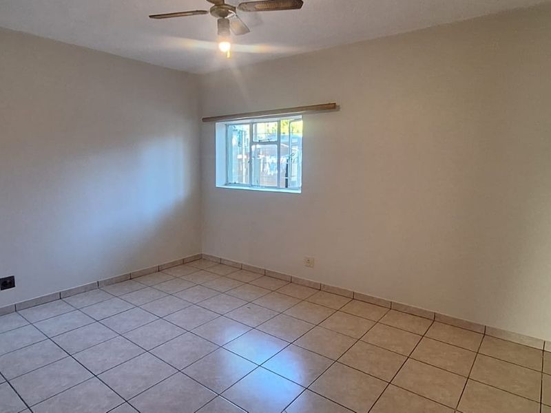 A clean, empty bedroom featuring neutral tiled flooring, a ceiling fan, and natural light from a window.