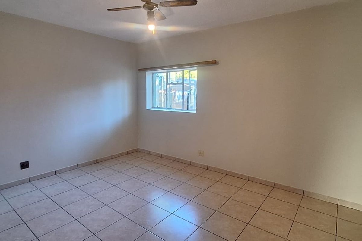 A clean, empty bedroom featuring neutral tiled flooring, a ceiling fan, and natural light from a window.