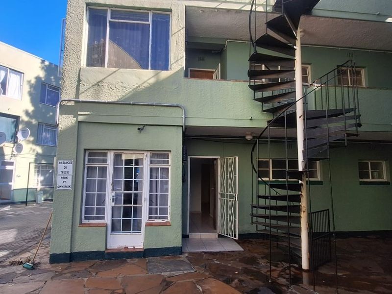 Rear exterior view of an apartment building featuring a metal spiral staircase, paved courtyard area, and security gate access.