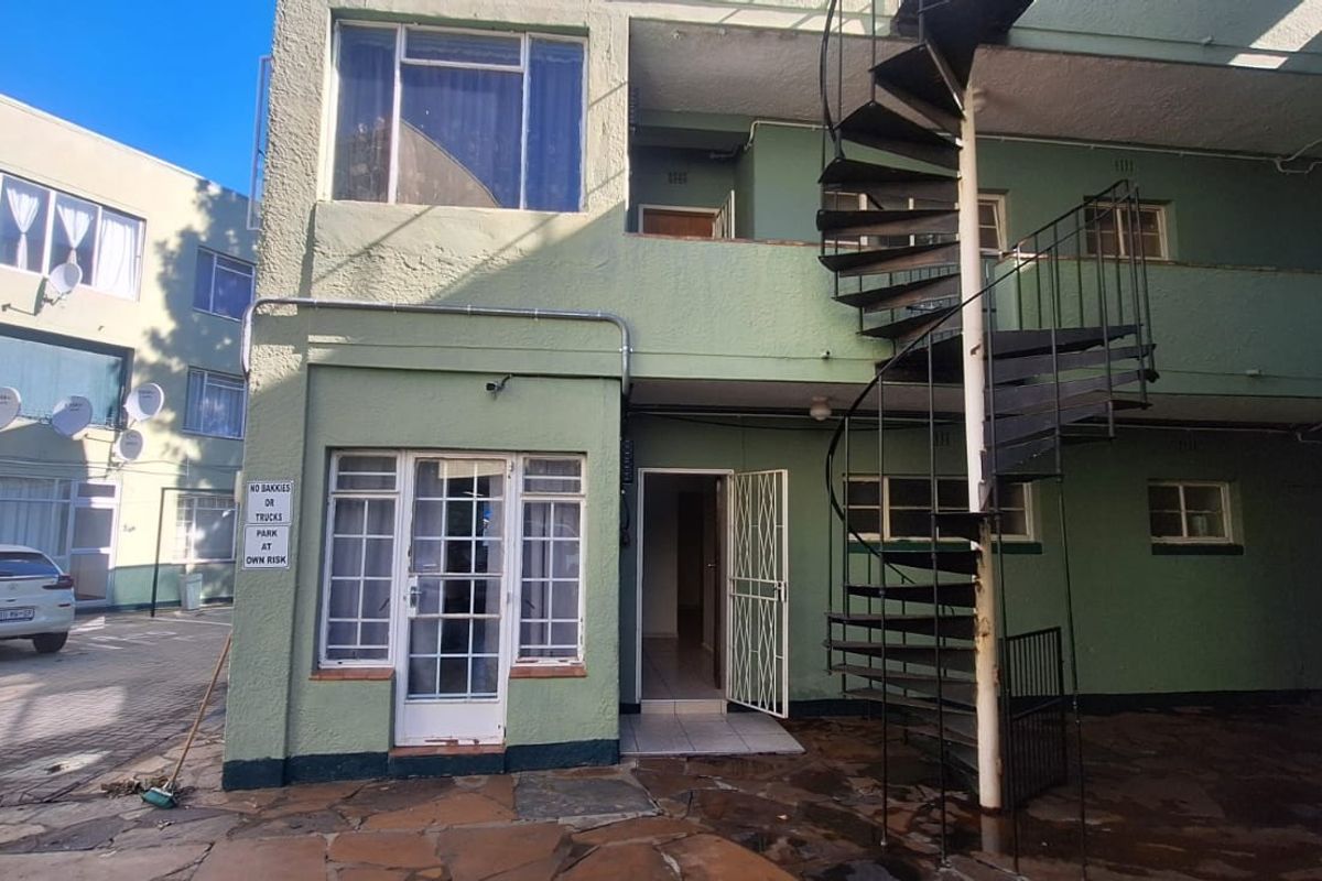 Rear exterior view of an apartment building featuring a metal spiral staircase, paved courtyard area, and security gate access.