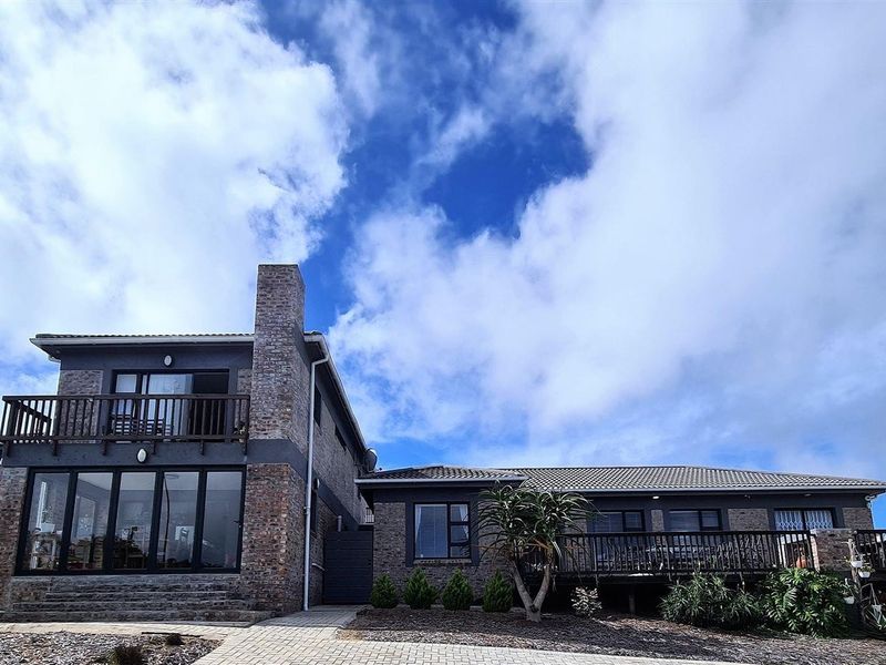 Rear view of a multi-level house featuring exposed brickwork, a timber balcony, and a paved walkway leading to the garden area.