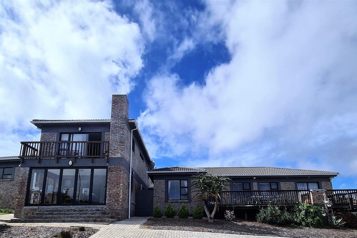 Rear view of a multi-level house featuring exposed brickwork, a timber balcony, and a paved walkway leading to the garden area.