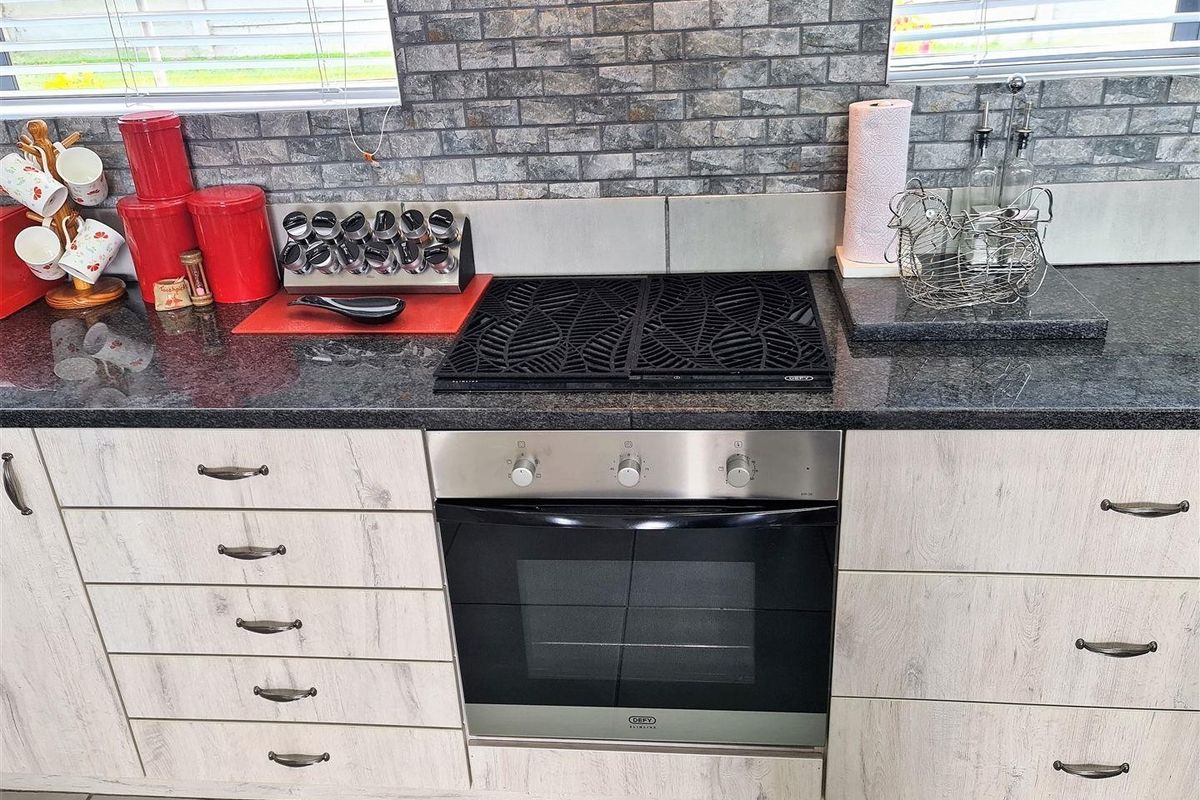 Modern kitchen featuring light wood-grain cabinetry, dark granite countertops, a built-in oven and hob, and a decorative stone-look tile backsplash.