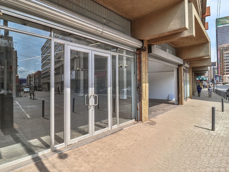 Commercial storefront featuring an aluminium-framed glass entrance with a security roller shutter, situated on a paved street-level sidewalk.