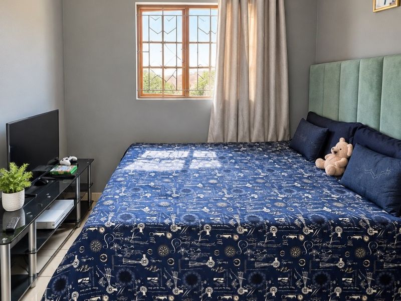 A well-maintained bedroom featuring neutral grey walls, large format floor tiles, and a window fitted with security bars.