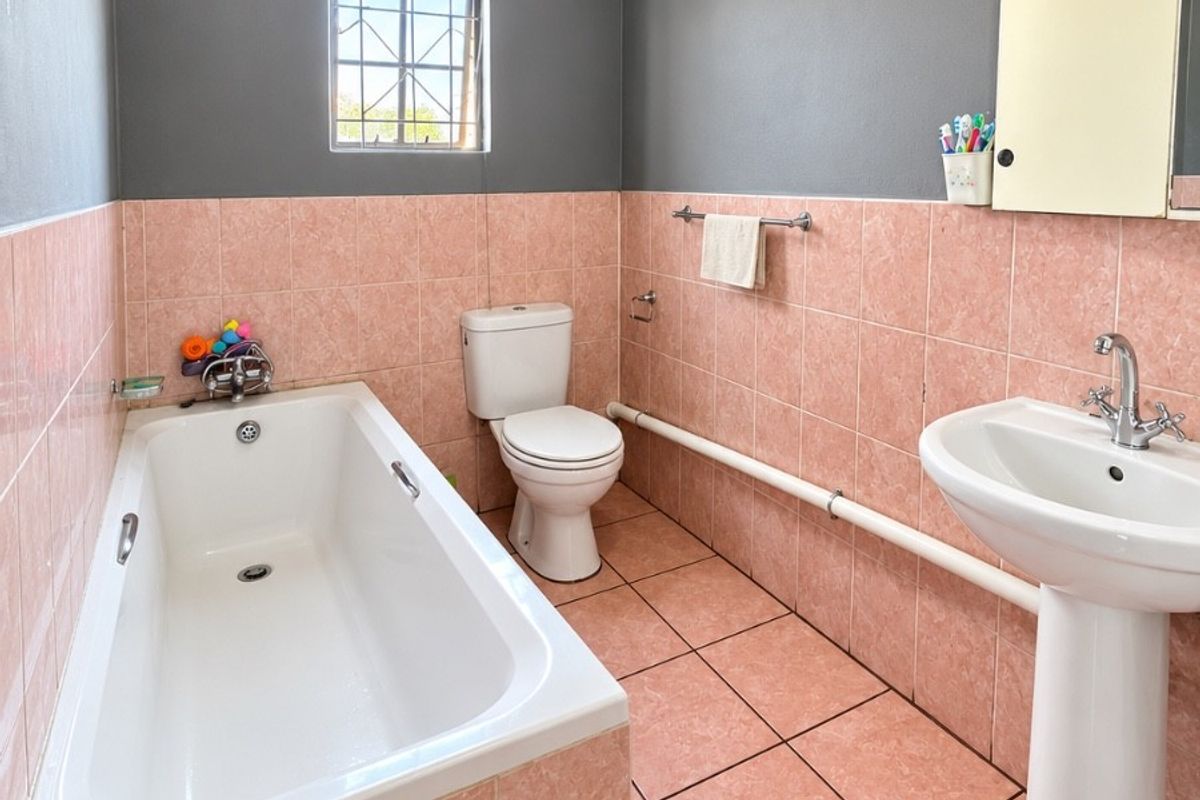 A functional bathroom featuring a bathtub, pedestal sink, and toilet, finished with pink wall and floor tiles and contrasting grey upper walls.
