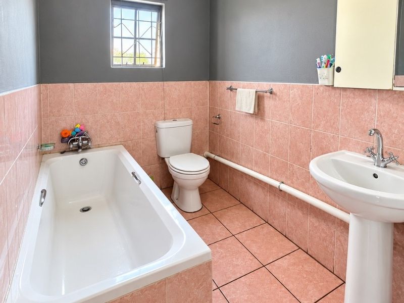 A functional bathroom featuring a bathtub, pedestal sink, and toilet, finished with pink wall and floor tiles and contrasting grey upper walls.