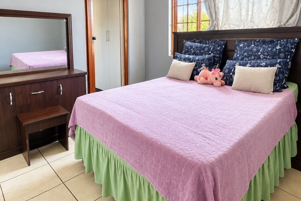 A well-lit bedroom featuring tiled flooring, a built-in cupboard, and a window with security bars, offering a functional and comfortable living space.