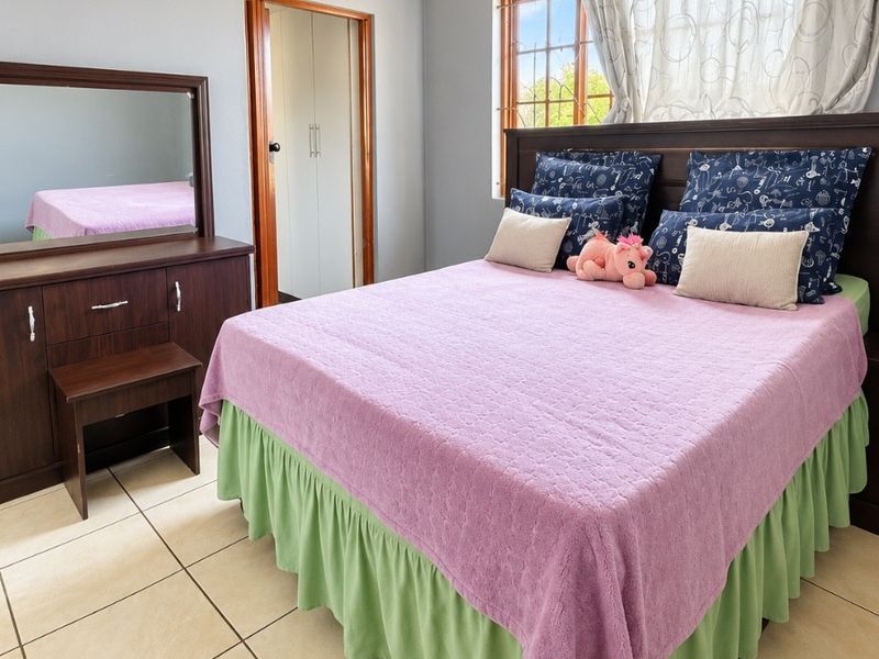 A well-lit bedroom featuring tiled flooring, a built-in cupboard, and a window with security bars, offering a functional and comfortable living space.