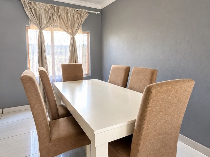 A well-maintained dining room featuring neutral grey walls, polished ceramic floor tiles, and a decorative recessed ceiling with crown molding.