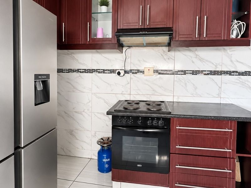 A well-maintained kitchen featuring dark wood cabinetry, marble-look wall tiling, built-in oven and hob, and modern ceramic floor tiles.