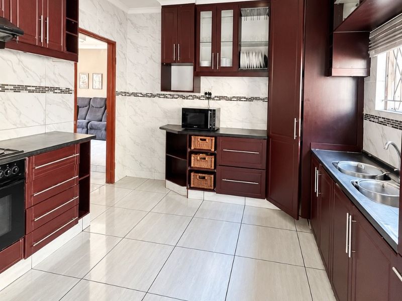 A well-maintained kitchen featuring dark wood cabinetry, stone countertops, a double basin sink, built-in oven, and modern tiled finishes throughout.