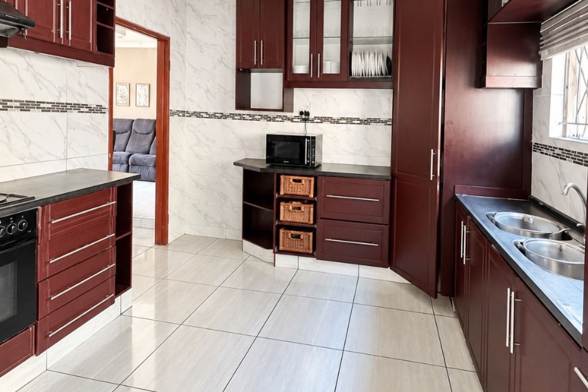 A well-maintained kitchen featuring dark wood cabinetry, stone countertops, a double basin sink, built-in oven, and modern tiled finishes throughout.